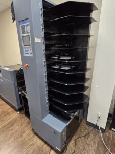 A tall office paper sorter with multiple trays beside a printer.