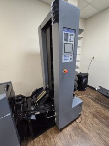 A tall, gray industrial machine with a control panel and cable connectors.
