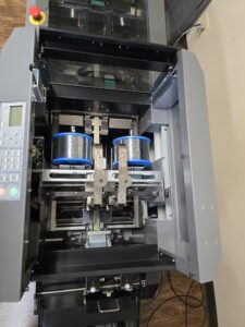 Industrial machine with robotic arms handling blue and white spools.